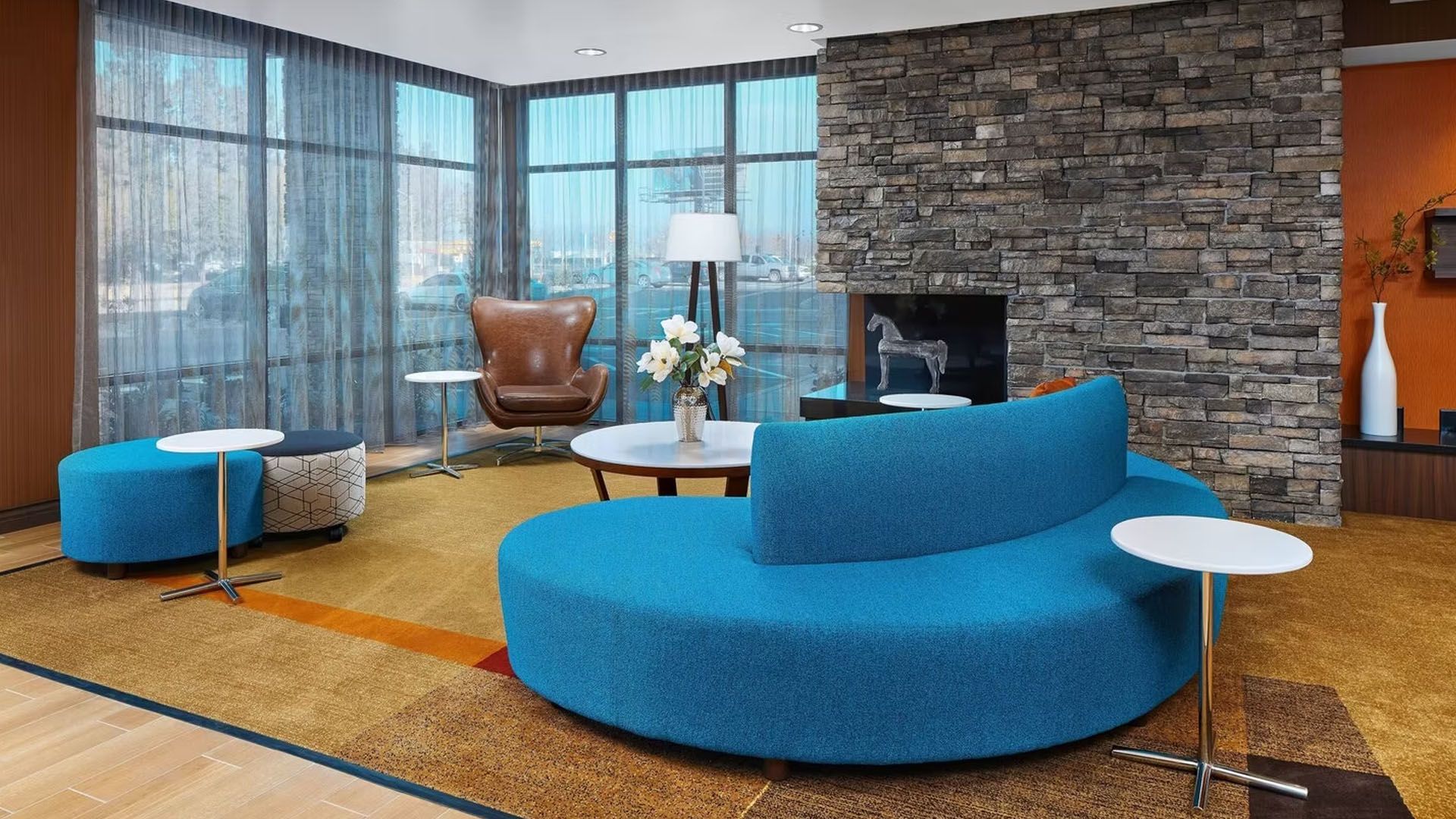 Lounge area with blue curved sofa, accent chairs, small tables, windows, and stone fireplace wall.