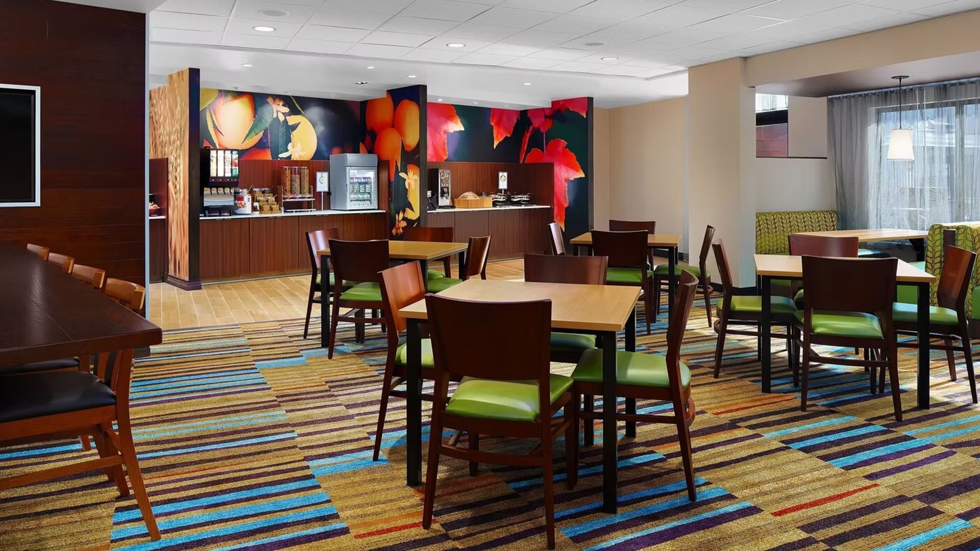 Hotel breakfast area with tables, chairs, and a buffet station with colorful wall art.