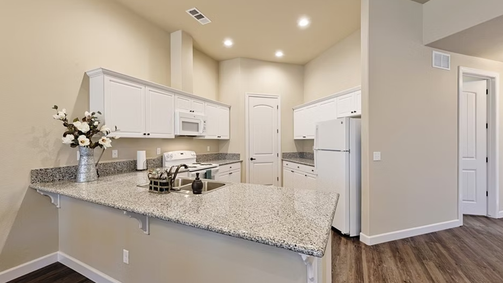 White kitchen with granite countertops, white appliances, and hardwood floors.