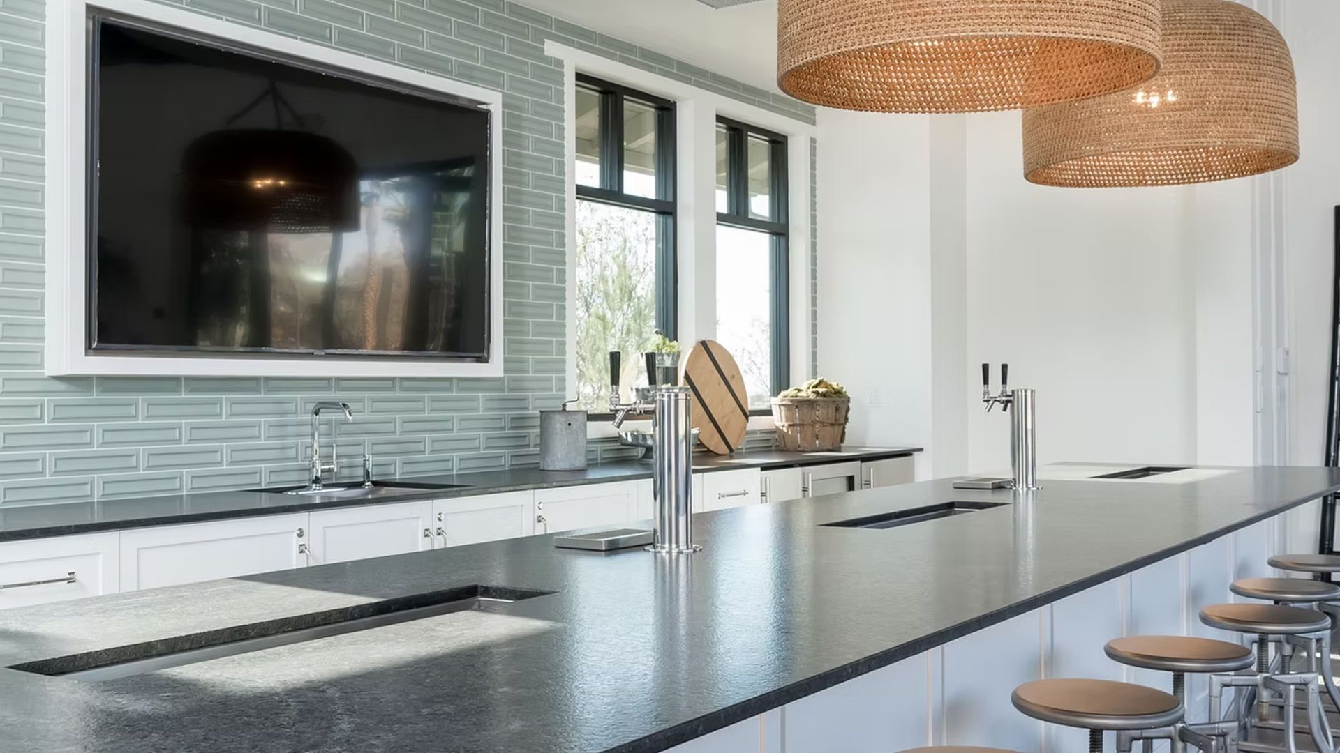 Modern kitchen with a long gray countertop bar, overhead lights, and a TV on the wall.