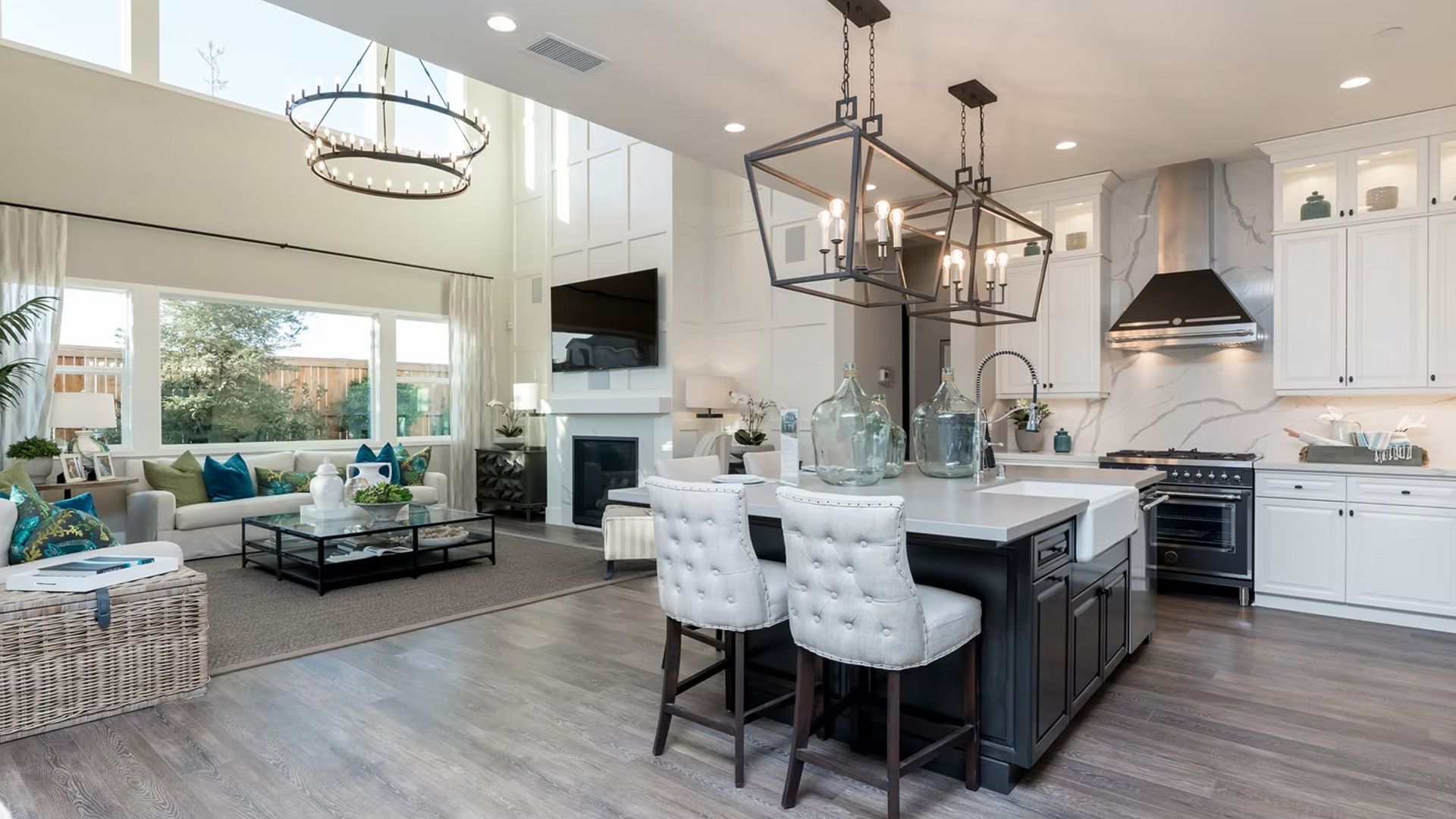 Open-concept kitchen and living room with island, fireplace, and high ceilings. White walls, grey flooring, and modern decor.