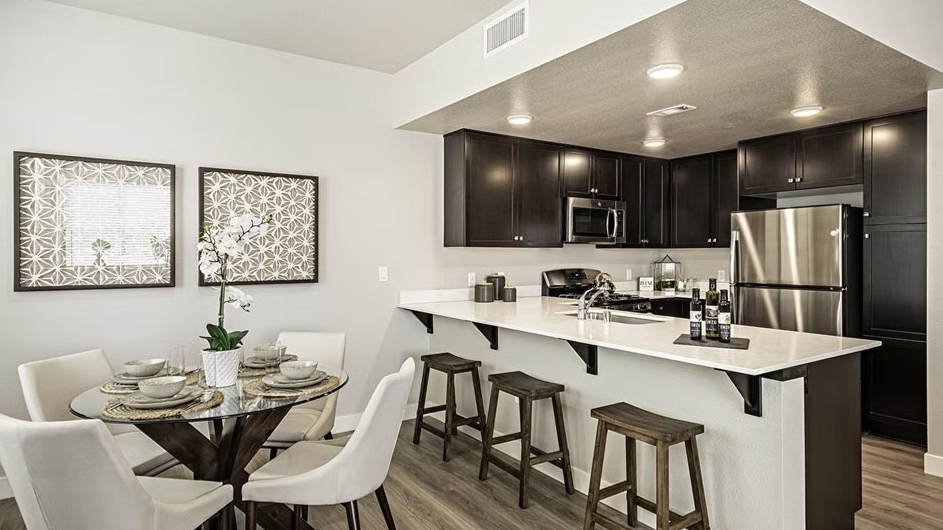 Modern kitchen and dining area with a breakfast bar, dark cabinets, and stainless steel appliances.