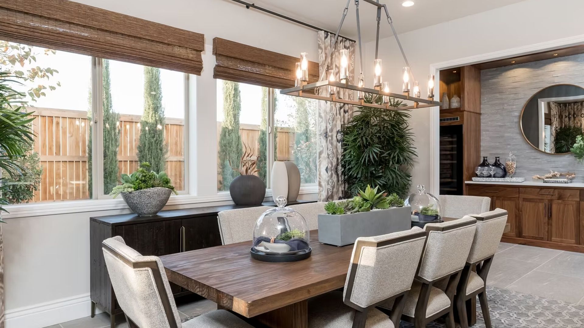 Dining room with wooden table and chairs, buffet, and large windows with outdoor view.