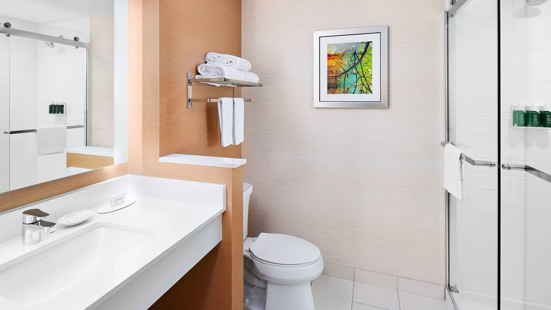 Bathroom with sink, toilet, and shower. Tan and white tones, art on the wall.