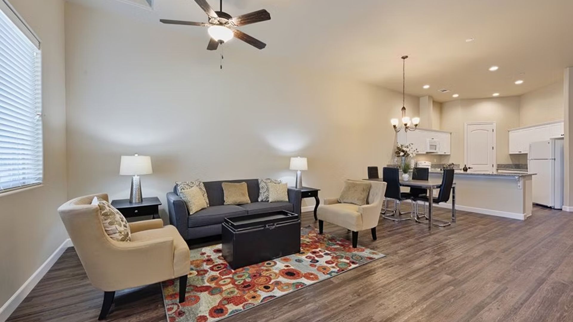 Open-concept living space with sofa, armchairs, and dining area; neutral tones, wood-look flooring.