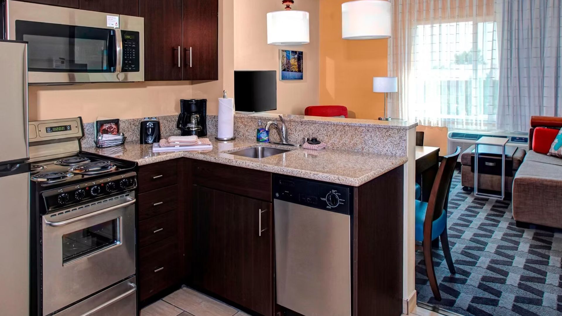 Kitchen area of a hotel room with stove, microwave, sink, and small dining area.