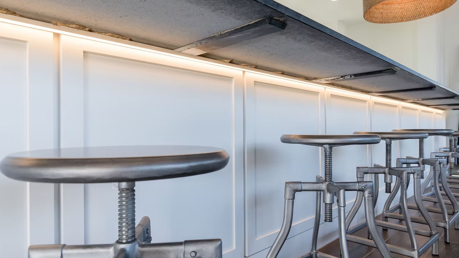 Row of industrial-style bar stools along a white paneled wall with under-counter lighting.