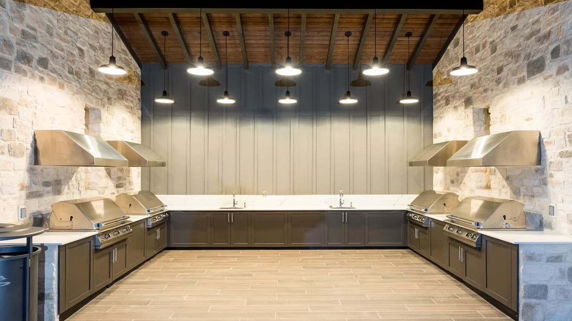 Outdoor kitchen with stainless steel grills, brick walls, and pendant lights.