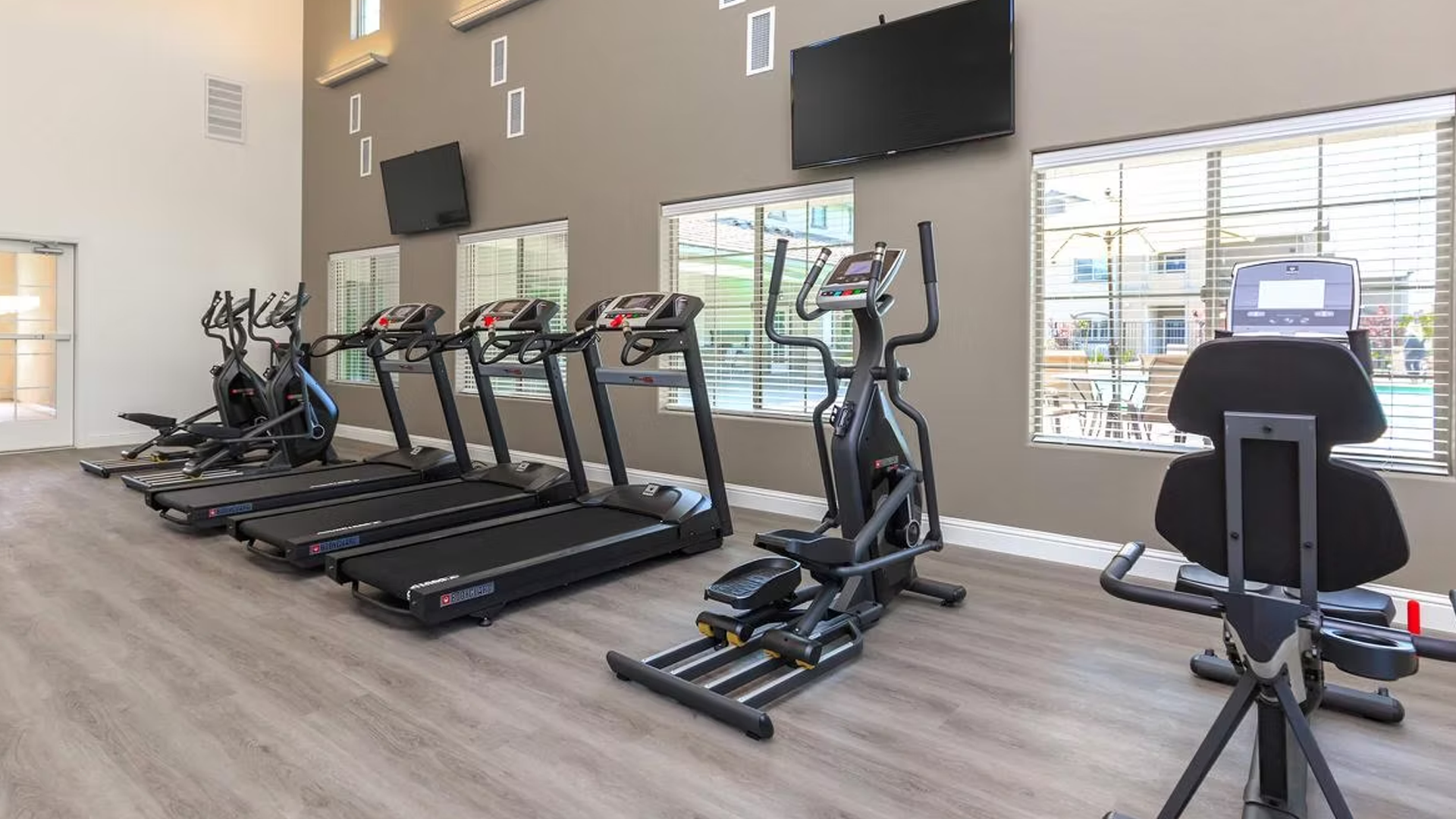 Gym with exercise equipment, including treadmills and stationary bikes, near windows and TVs.