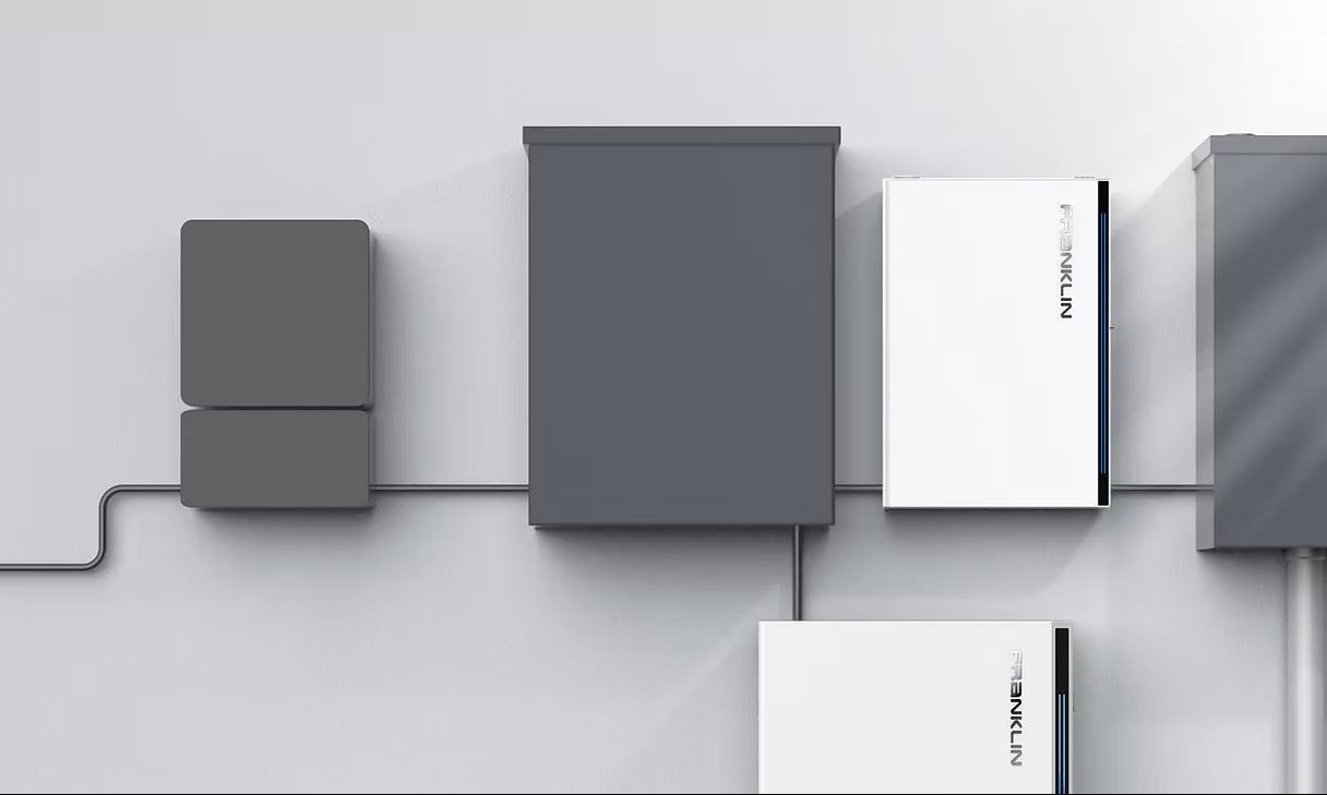 Solar energy equipment mounted on a white wall, consisting of gray and white boxes and wiring.