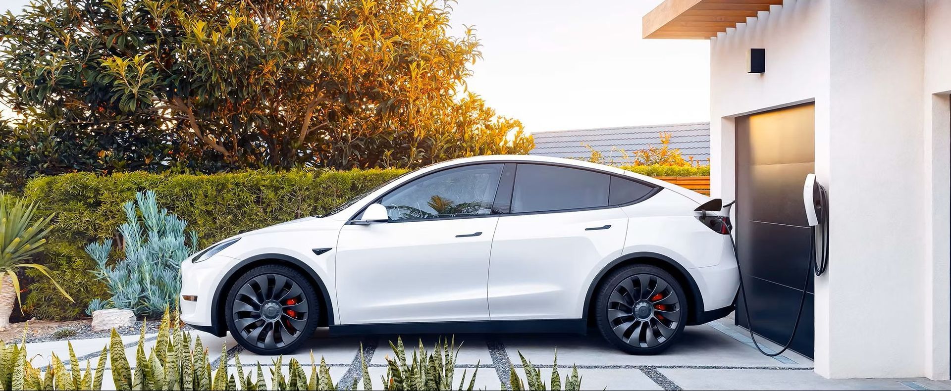 White Tesla electric car parked next to a garage, charging.