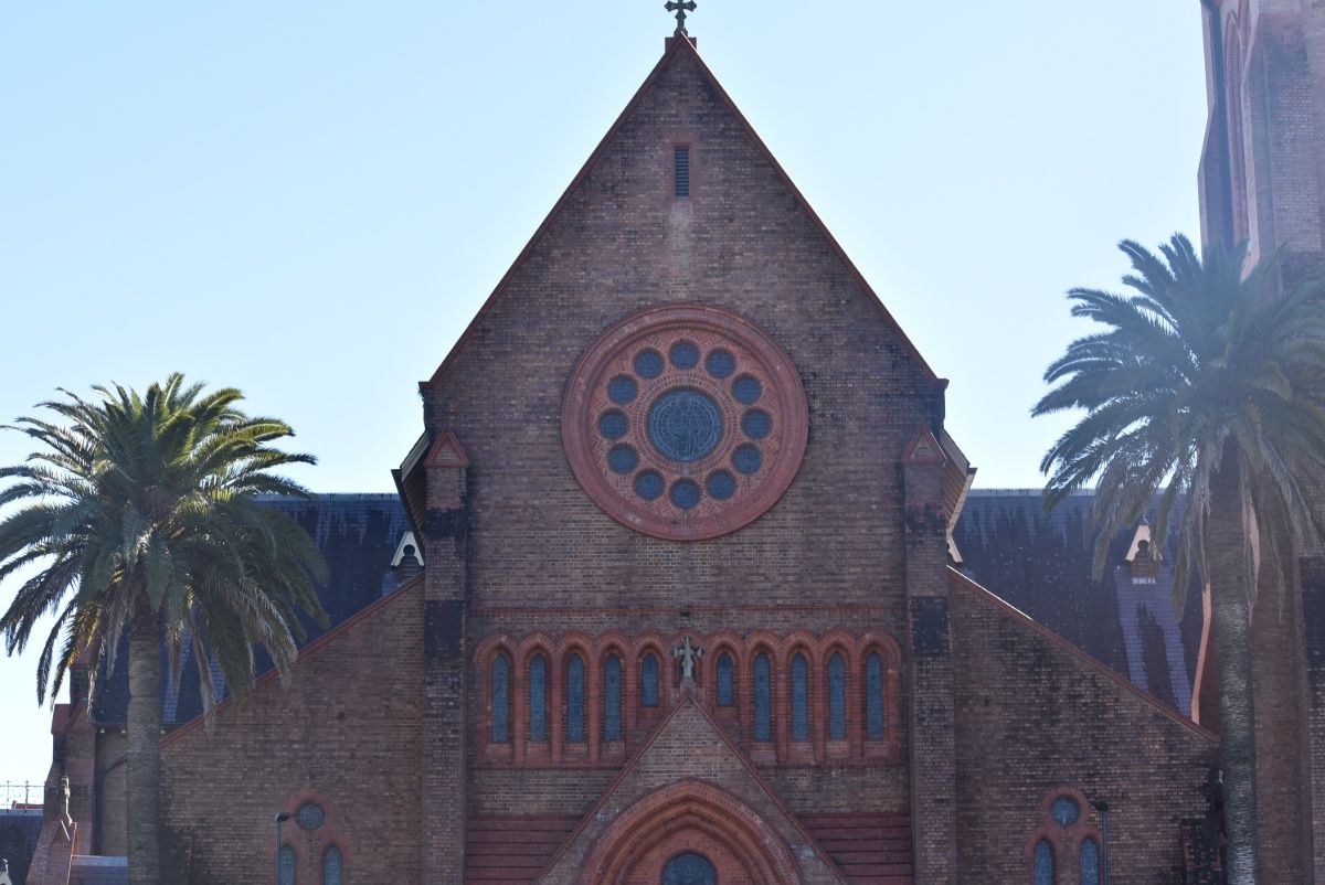 Brick church with arched windows, a rose window, and palm trees against a blue sky — Superior Wifi in Lismore, NSW