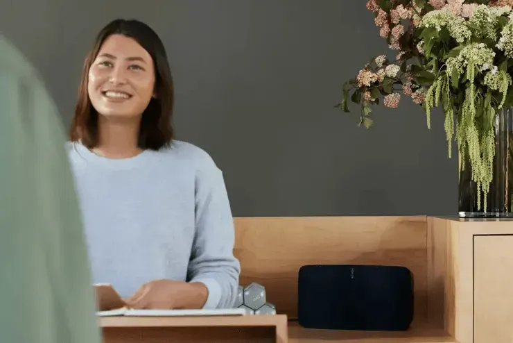 Woman Smiles, Holding Card at Desk, Next to Speaker and Flowers — Superior Wifi in East Ballina, NSW