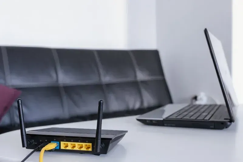 Black Router With Two Antennas and a Connected Laptop on a White Table Near a Black Sofa — Superior Wifi in Ballina, NSW