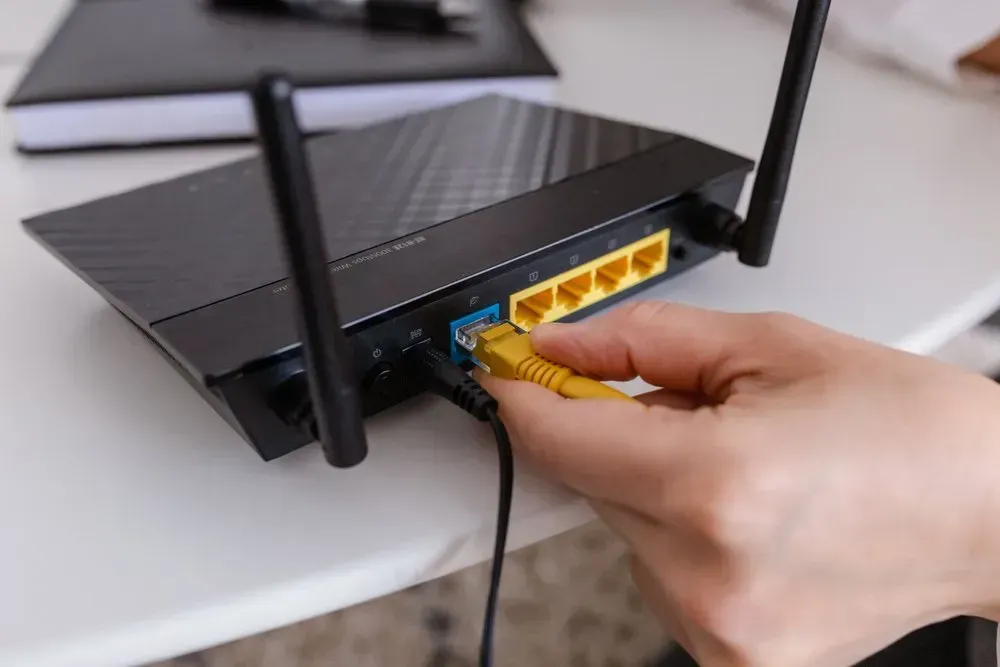 Hand Plugging a Yellow Ethernet Cable Into the Back of a Black Wi-fi Router — Superior Wifi in Byron Bay, NSW