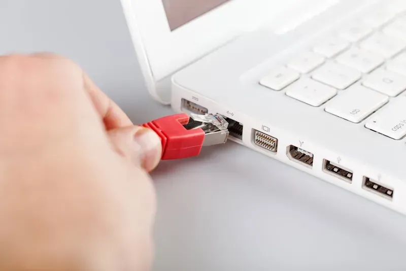 Hand Plugging a Red Ethernet Cable Into a White Laptop — Superior Wifi in Byron Bay, NSW