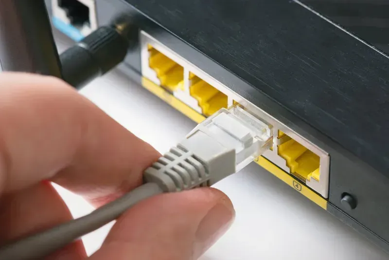 Hand Plugging a Grey Ethernet Cable Into a Yellow Port on a Black Router — Superior Wifi in Ballina, NSW