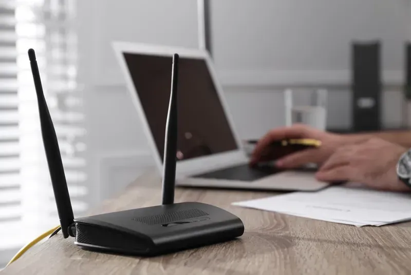 Black Wireless Router With Antennae on Desk, Laptop and Person — Superior Wifi in Byron Bay, NSW