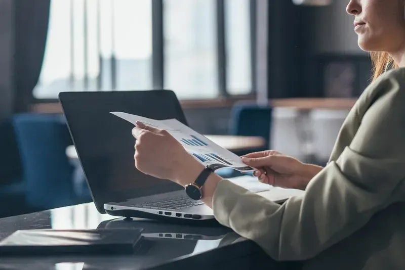 Woman Reviewing Document With Charts, Using Laptop in a Modern Office Setting — Superior Wifi in Byron Bay, NSW