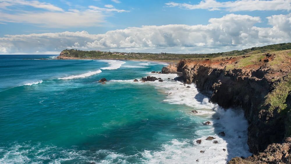 Ocean Waves Crash Against a Rocky Cliff Under a Blue Sky With White Clouds — Superior Wifi in Lennox Head, NSW