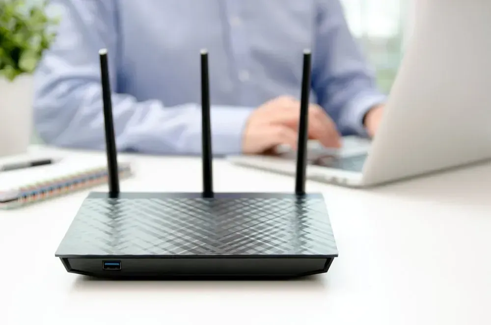 Black Wi-fi Router With Three Antennas on a White Desk; a Person Uses a Laptop — Superior Wifi in Ballina, NSW