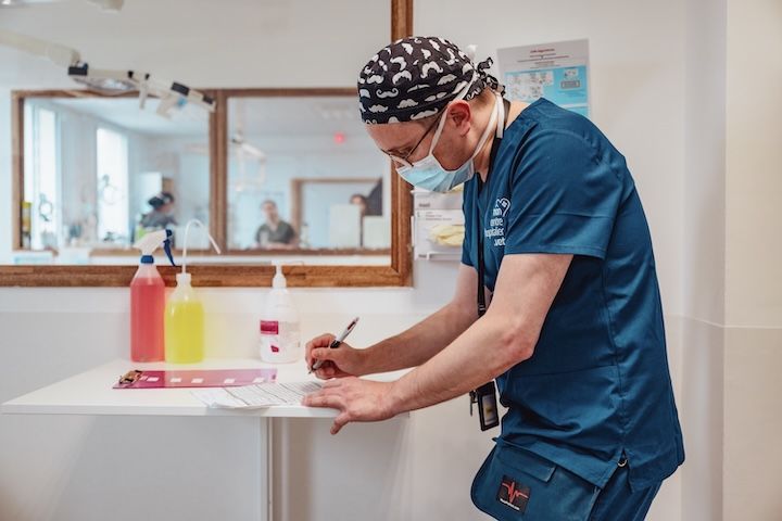 Un chirurgien portant un masque et une blouse écrit sur un morceau de papier.