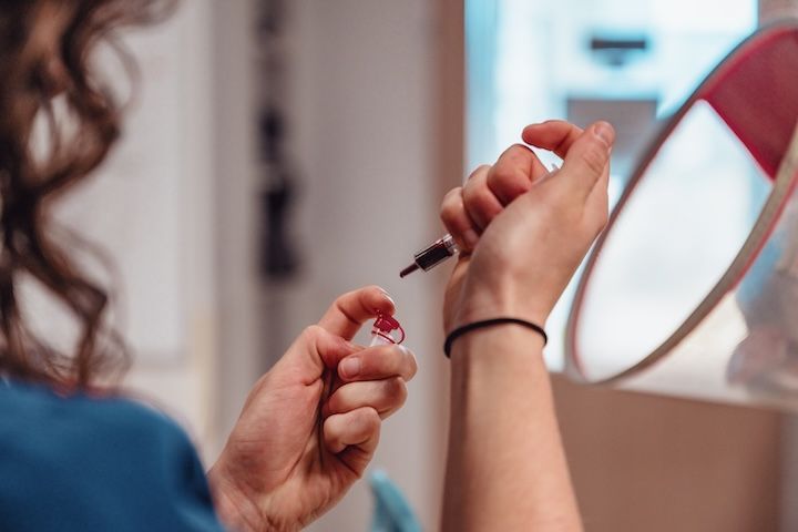 Une femme applique du vernis à ongles sur ses ongles devant un miroir.