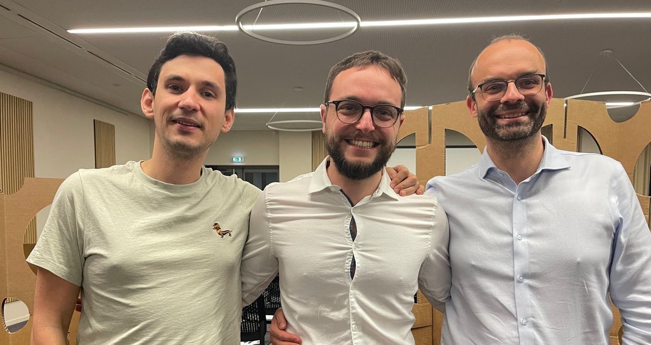 Trois hommes posent pour une photo ensemble dans une pièce.