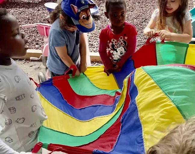 Children holding a colorful parachute; outdoors.
