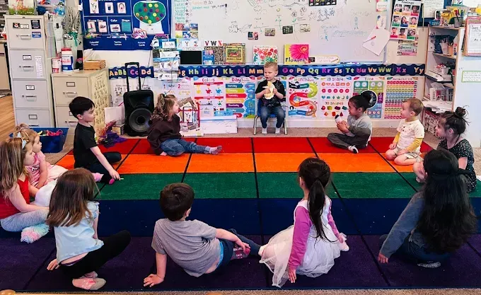 Children sitting in a circle on a colorful mat, one playing a flute, in a classroom.
