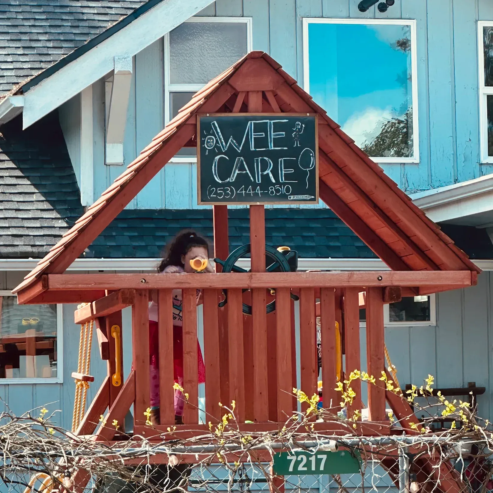 A little girl is playing on a wooden playground with a sign that says wee care