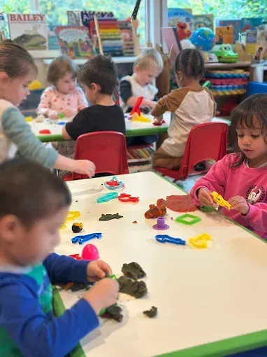 Children at tables play with colorful playdough in a classroom.