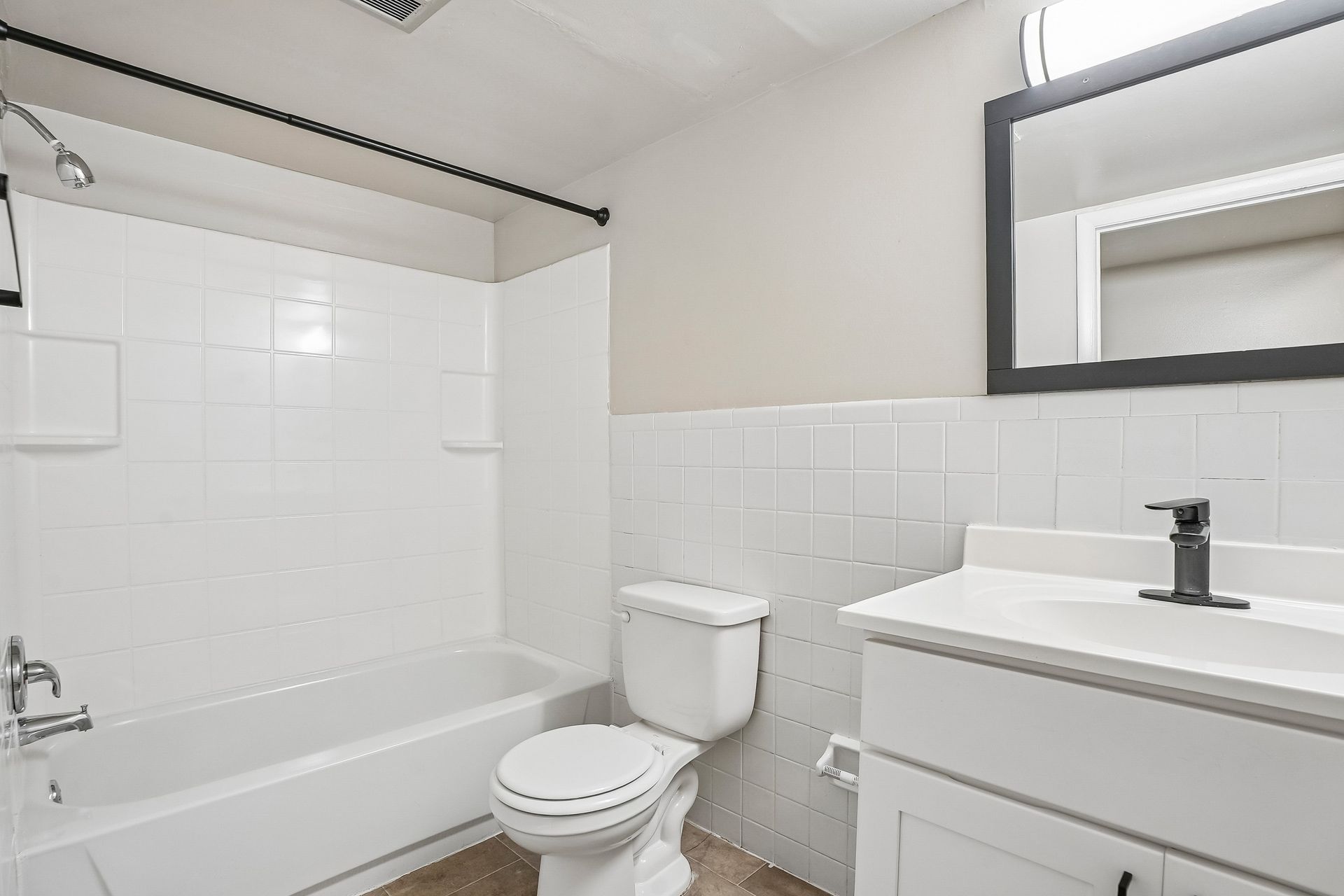 White bathroom with tub, toilet, and vanity sink, viewed from the doorway.