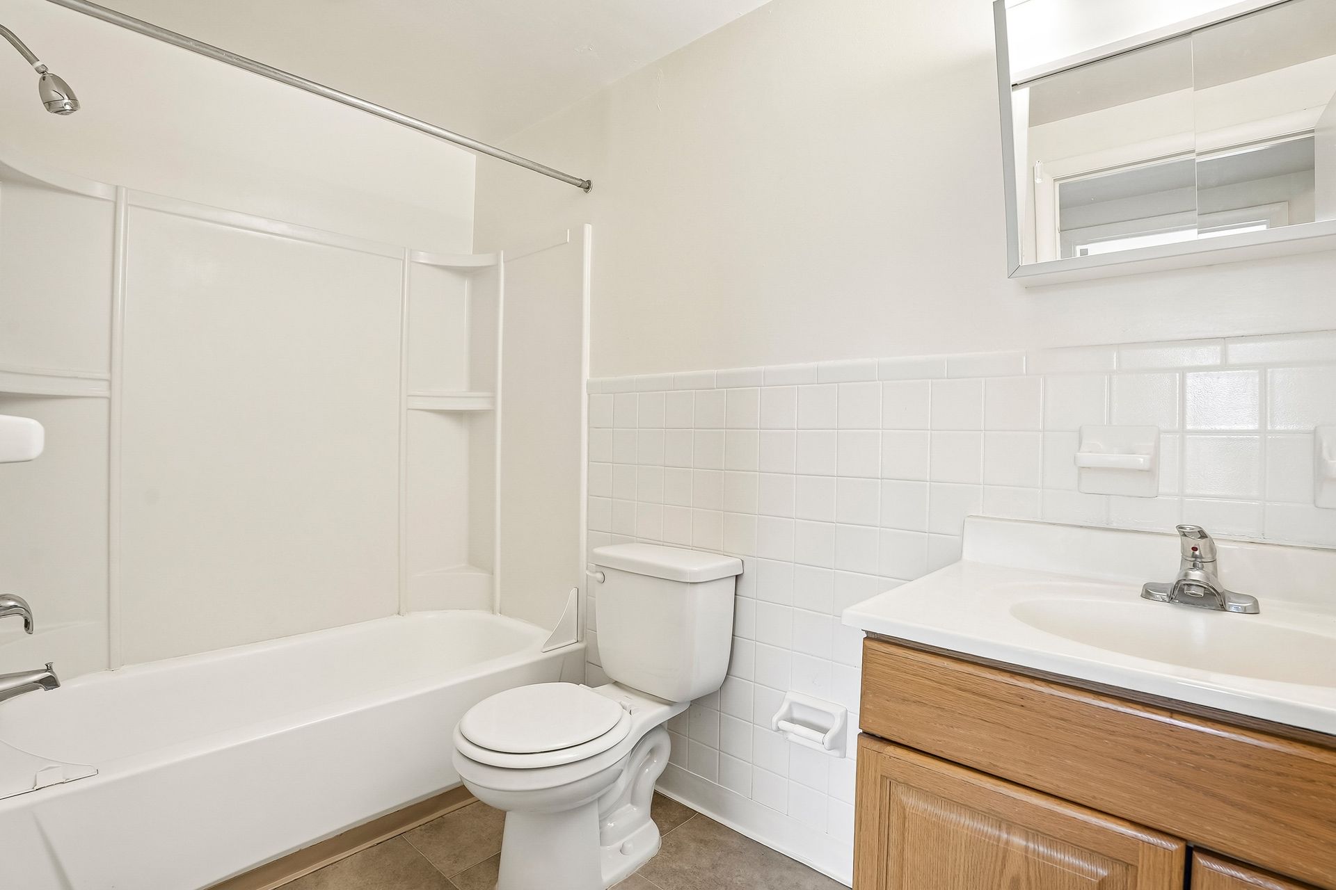 Bright bathroom with white tub, toilet, tiled walls, and wood vanity with sink