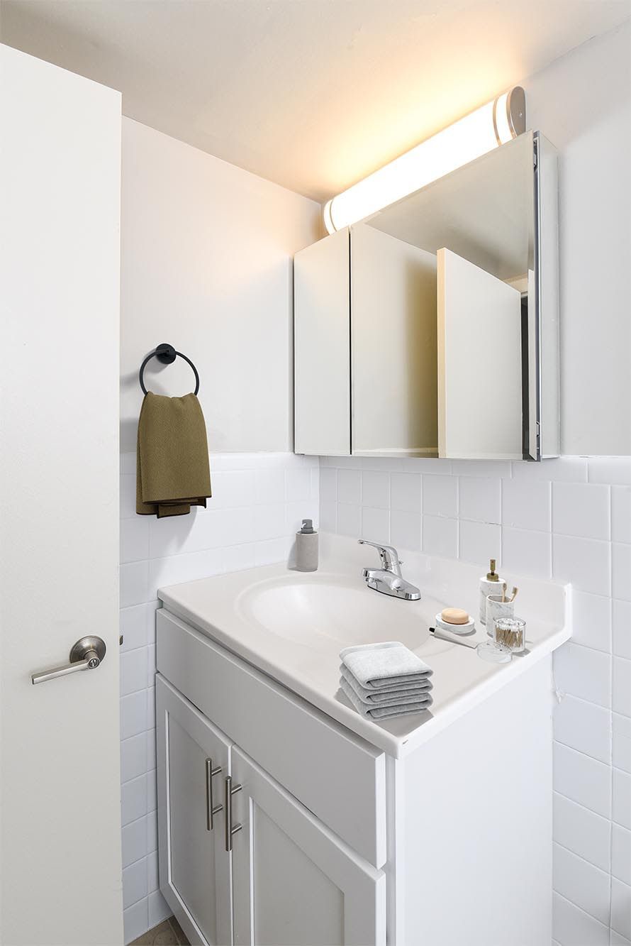 White bathroom vanity with sink, mirrored medicine cabinet, towel ring, and folded towels at Westover Pointe in Wilmington, DE.