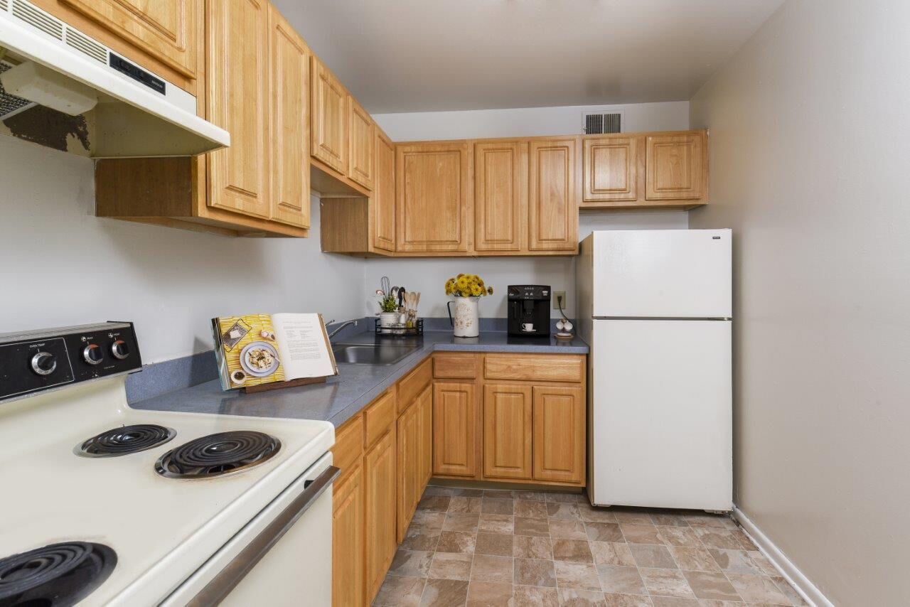 Kitchen in an apartment with light wood cabinets, gray countertops, a stove, sink, and a white refrigerator at Westover Pointe in Wilmington, DE.