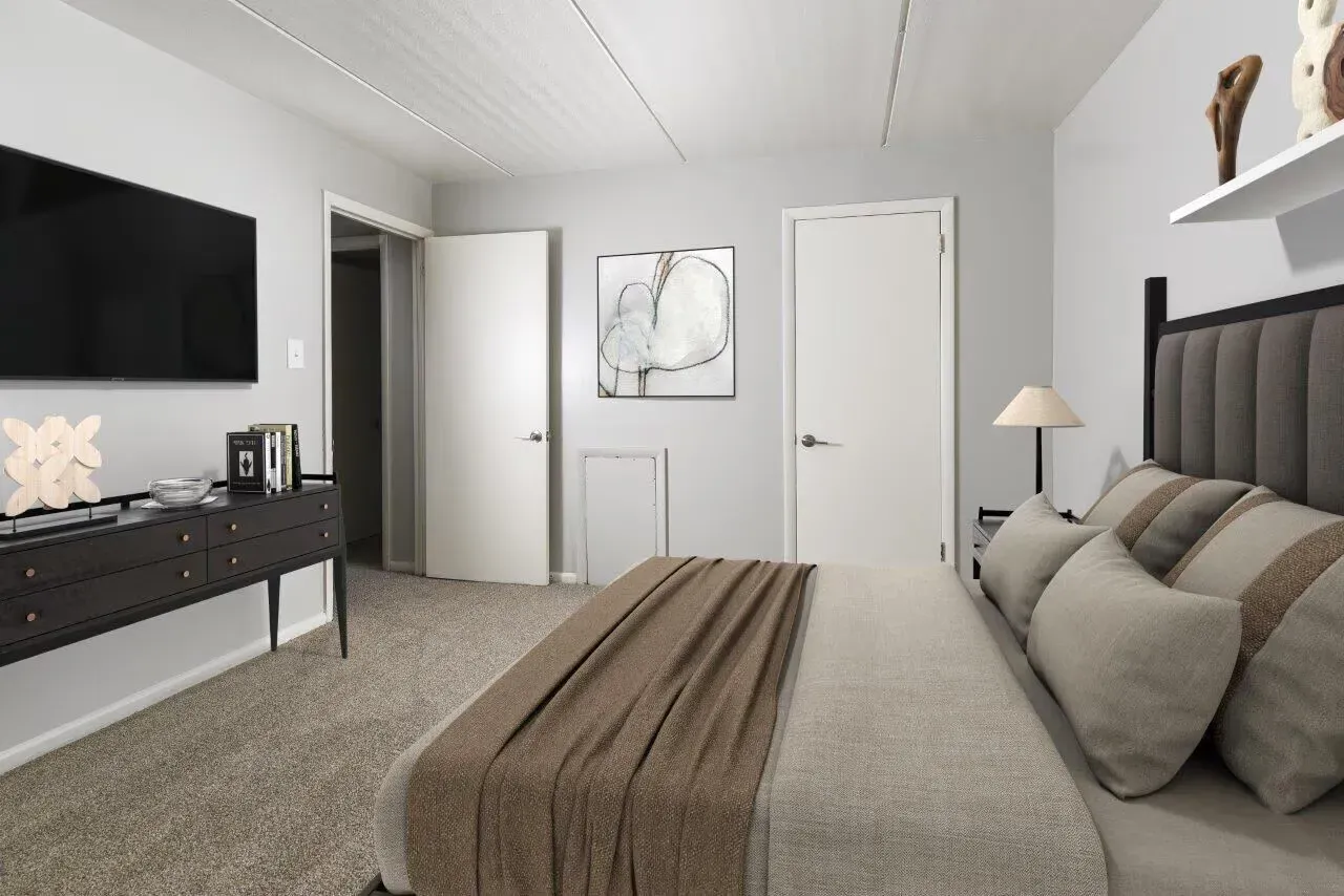 Bedroom with a large upholstered bed, dresser, wall-mounted TV, and neutral decor at Westover Pointe in Wilmington, DE.