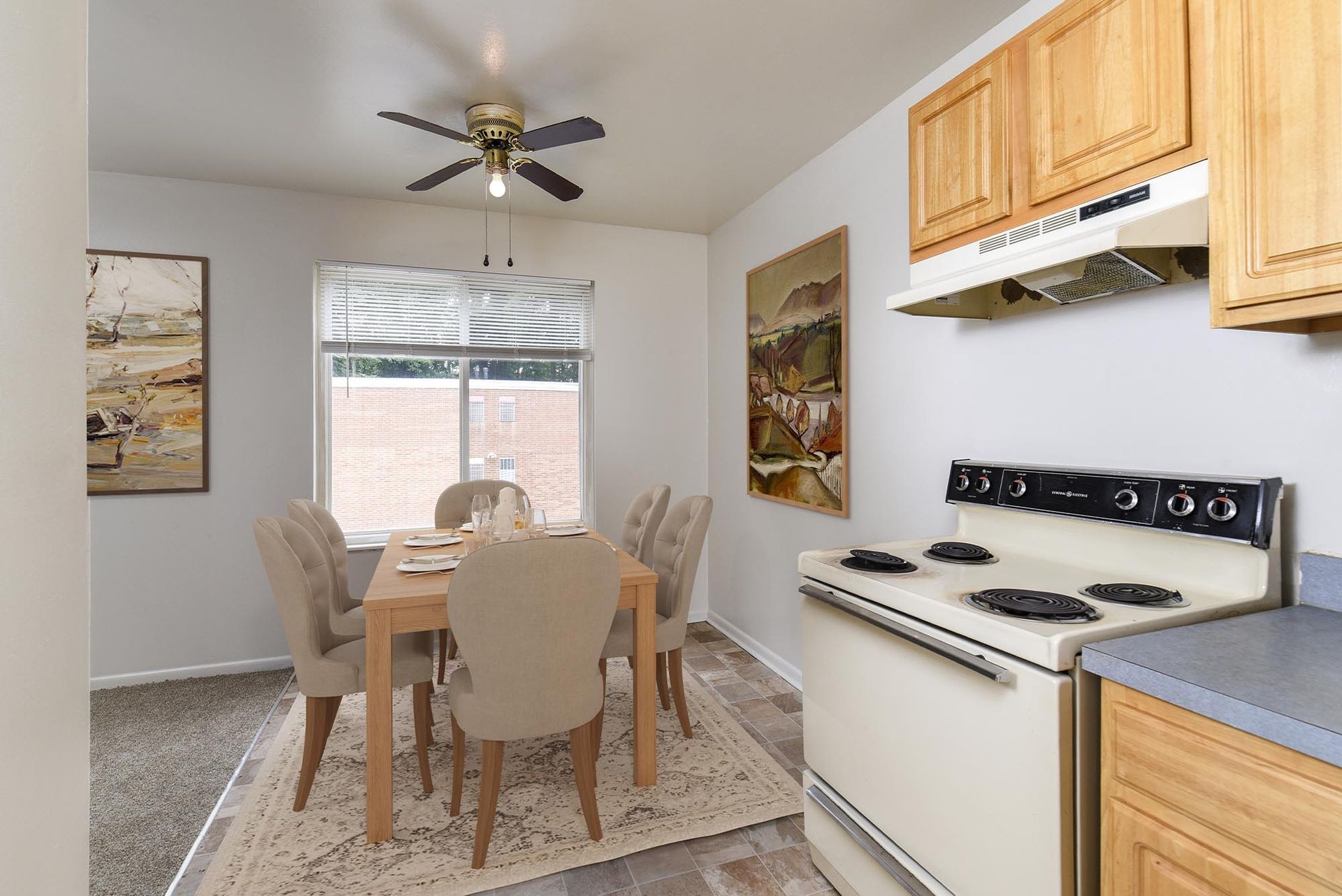 Apartment dining area with wooden table, beige upholstered chairs, window, ceiling fan, and stove at Westover Pointe in Wilmington, DE.