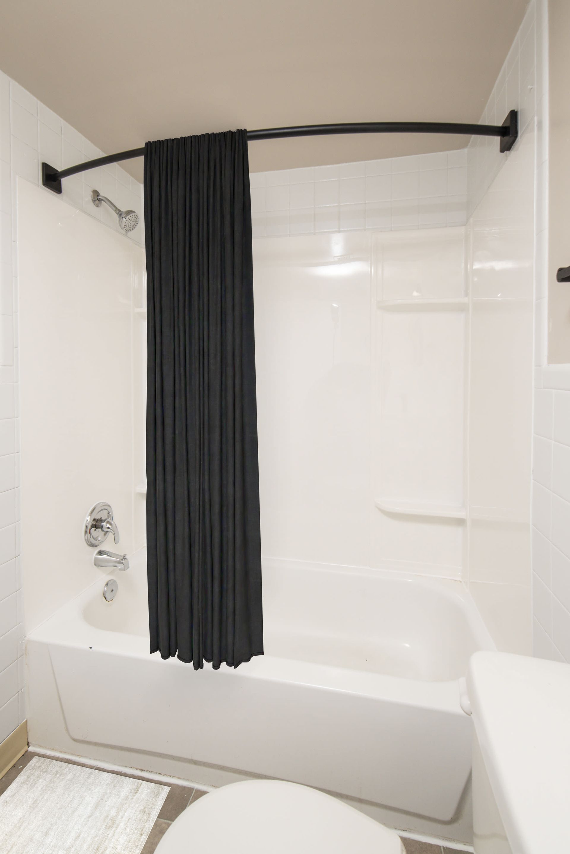 White tiled bathroom with bathtub/shower, curved black rod, and black curtain at Westover Pointe in Wilmington, DE.