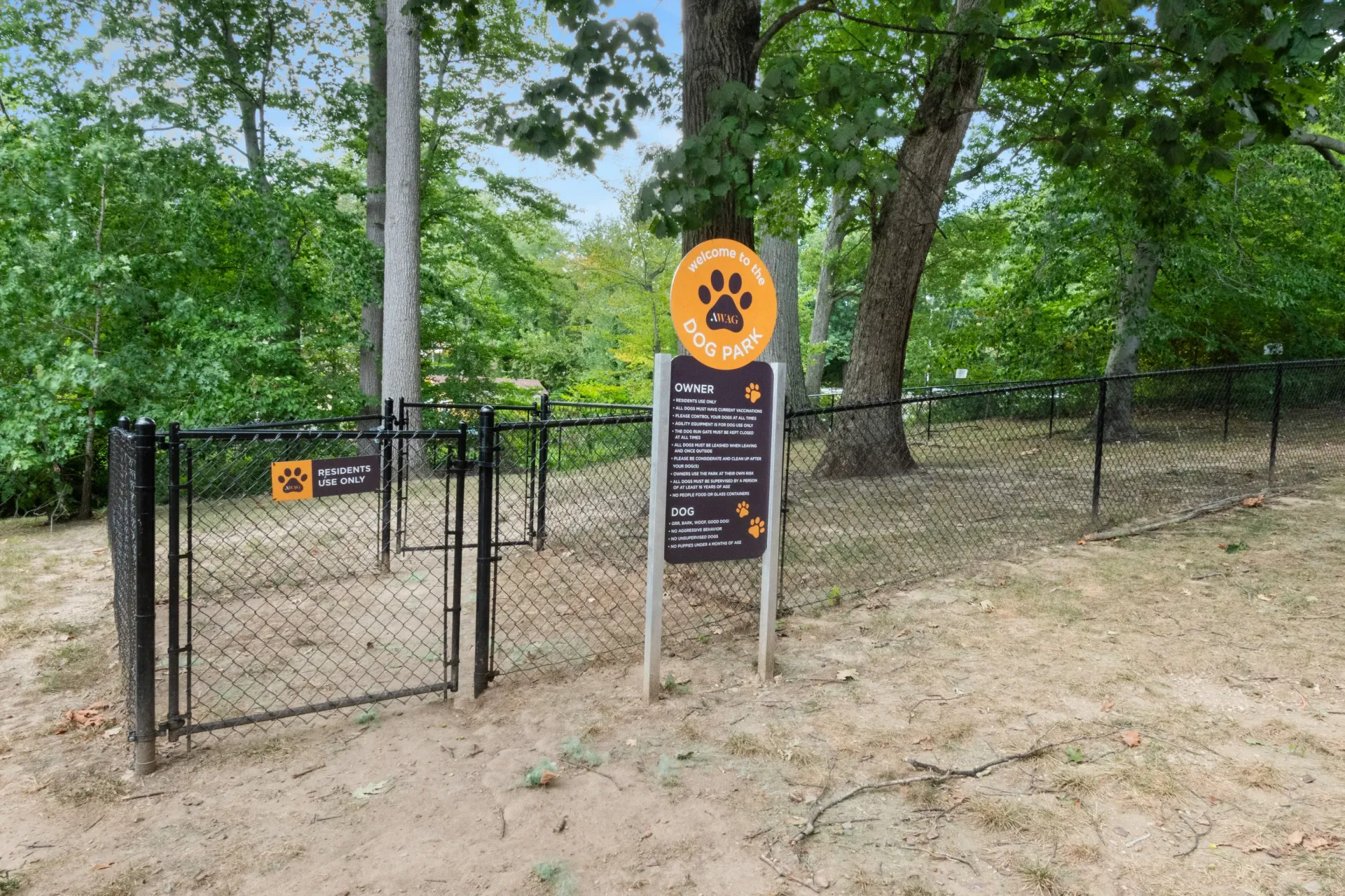 Fenced dog park area with orange dog park sign and information plaque among trees at Westover Pointe in Wilmington, DE.