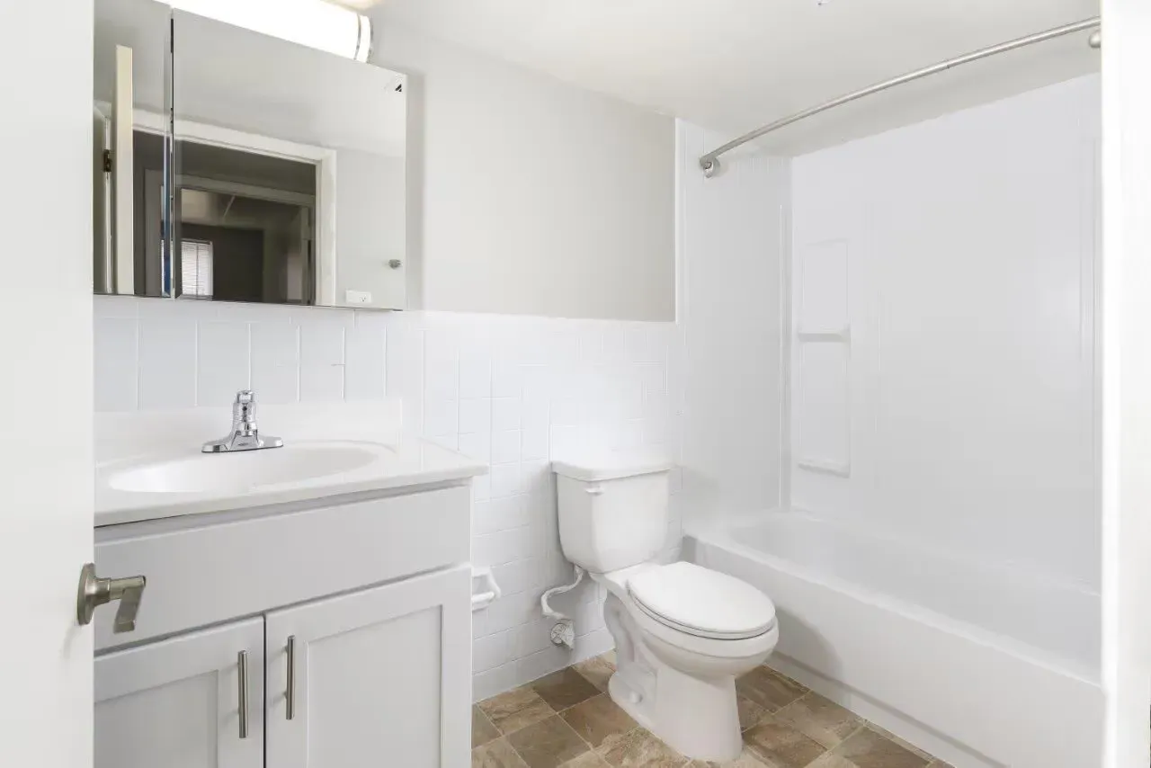White bathroom with vanity, toilet, and bathtub with curved shower rod at Westover Pointe in Wilmington, DE.