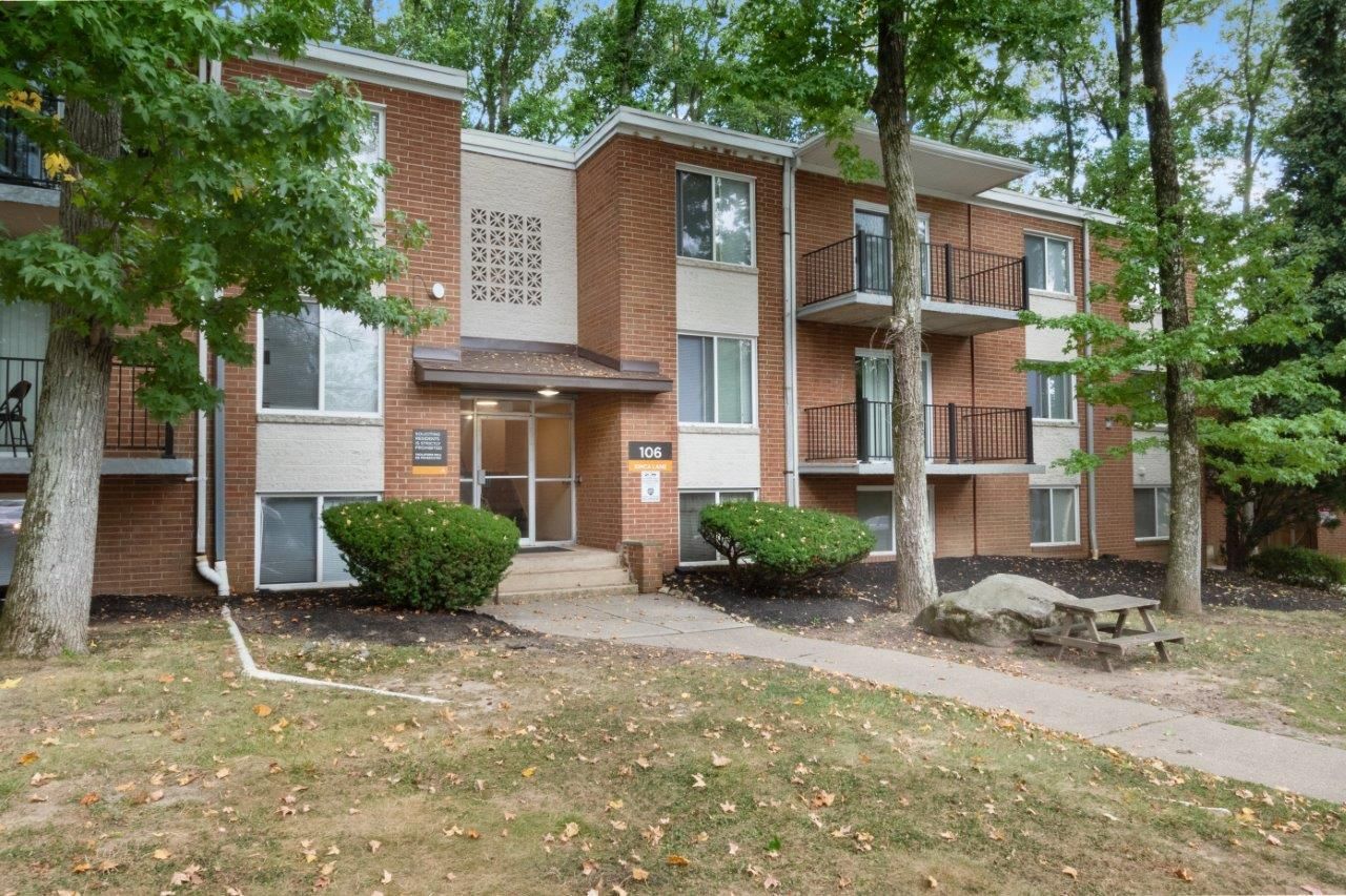 Exterior view of a brick apartment building with trees, a walkway, and balconies at Westover Pointe in Wilmington, DE.