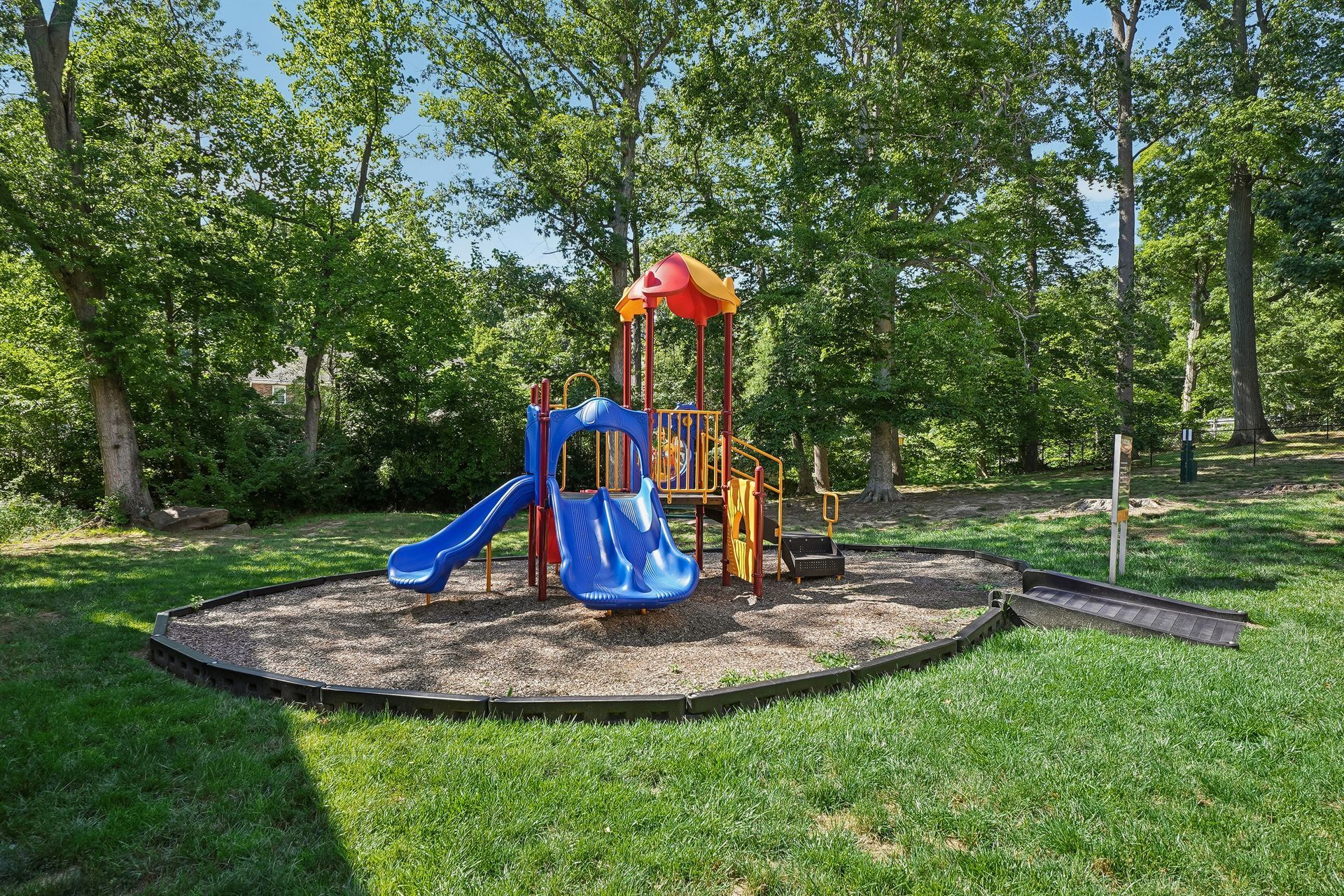 Colorful playground set with blue slide and orange canopy on a grassy park surrounded by trees