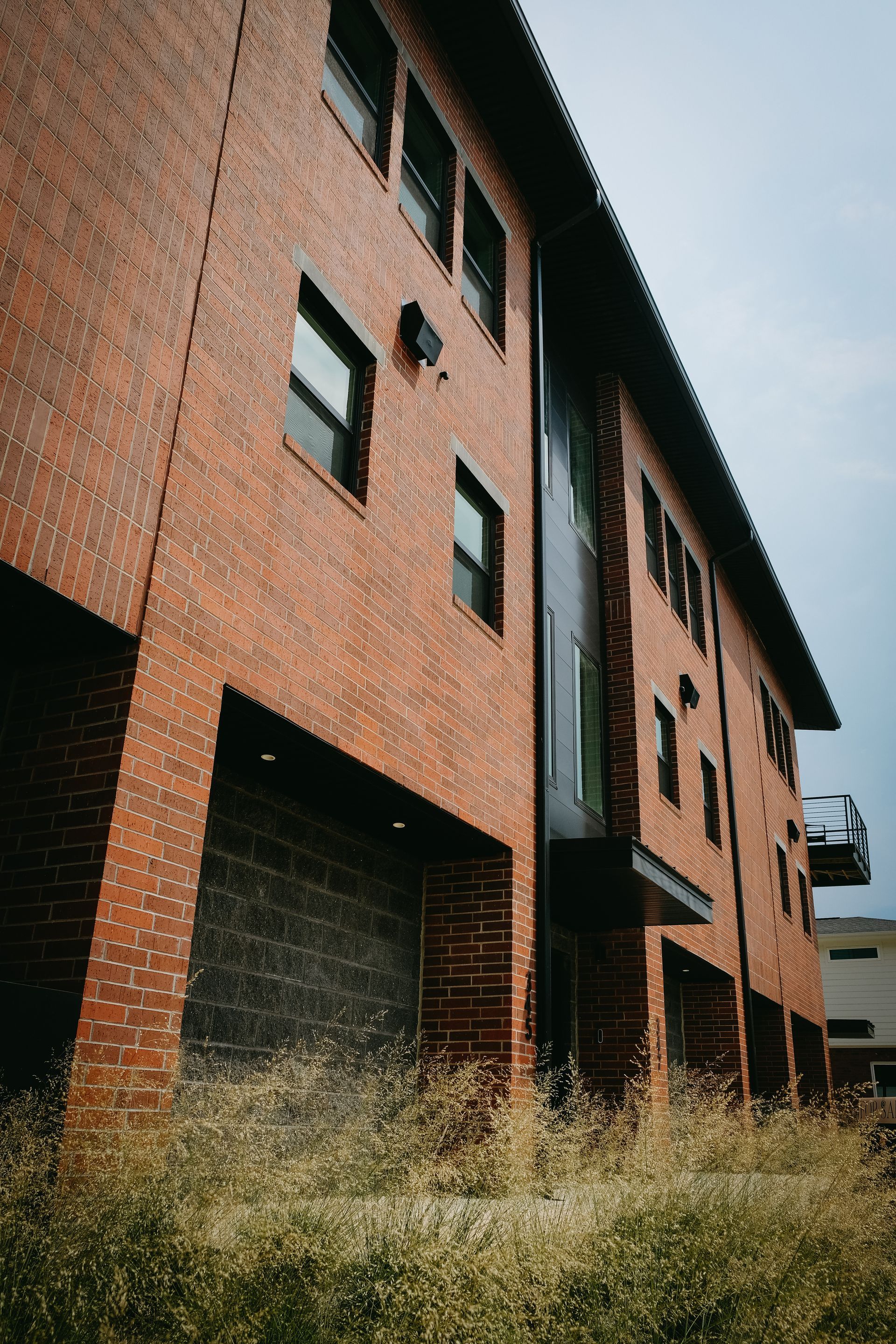 A large brick building with a lot of windows is surrounded by tall grass.