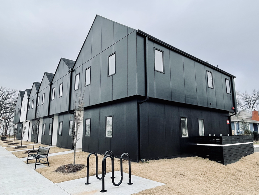 A row of black buildings with a bike rack in front of them.