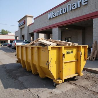 Yellow dumpster overflowing with wood in front of a store with red trim.