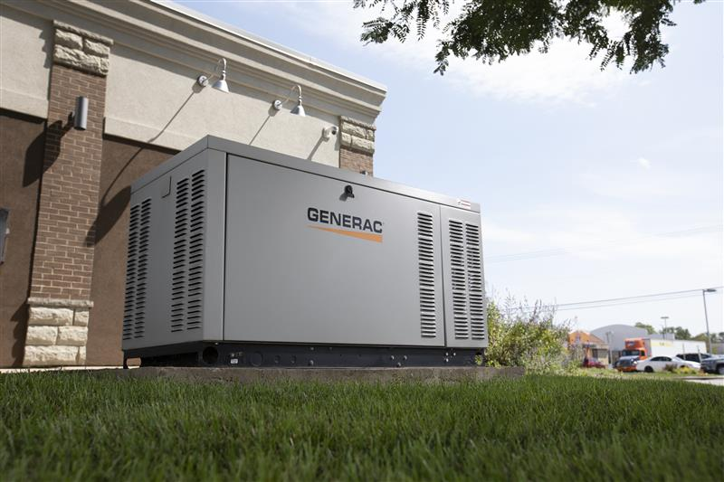 Portable generator beside a building, with grass in the foreground and a road in the background