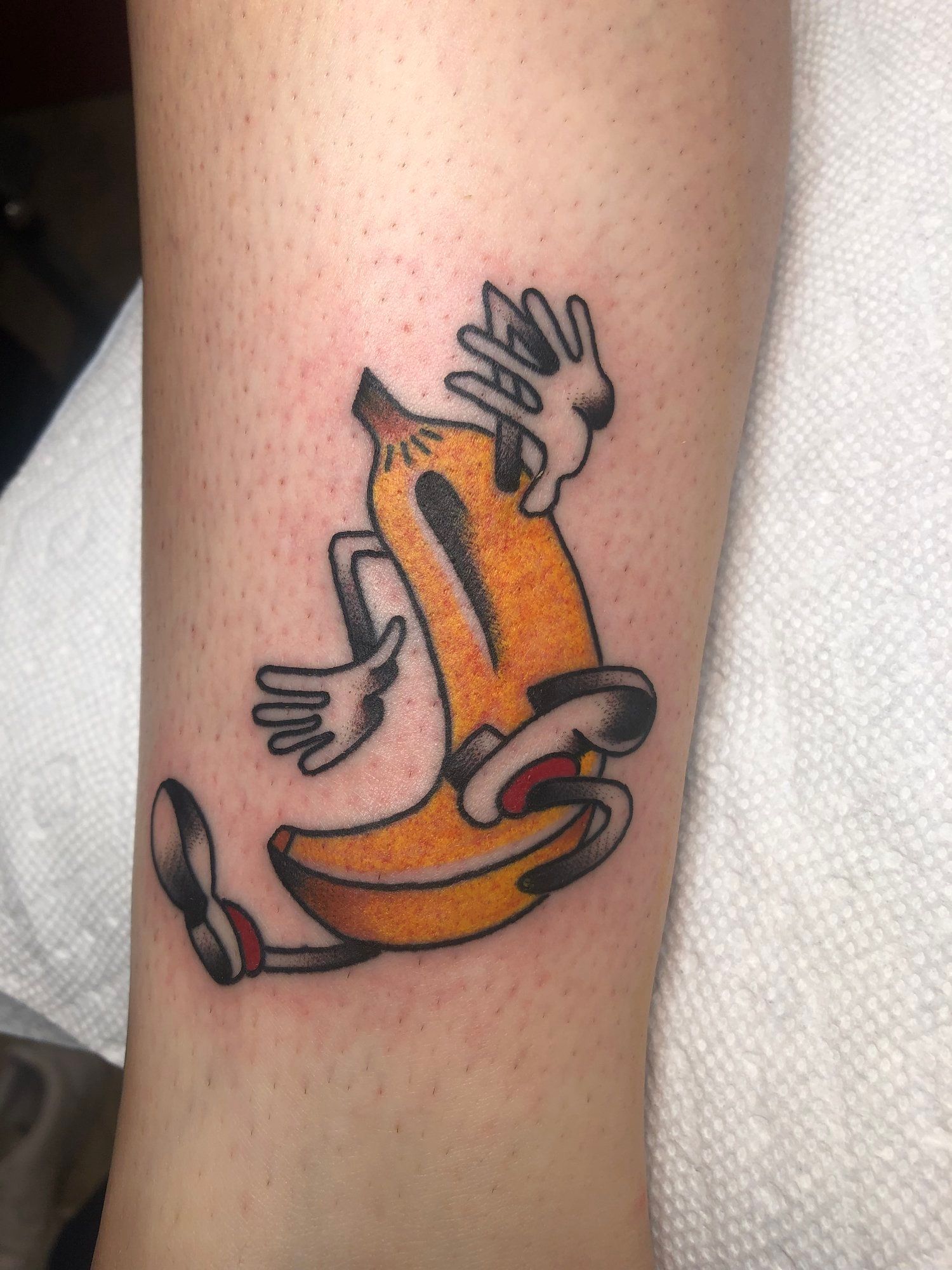 A tattoo of a banana with hands and legs on a person 's arm.