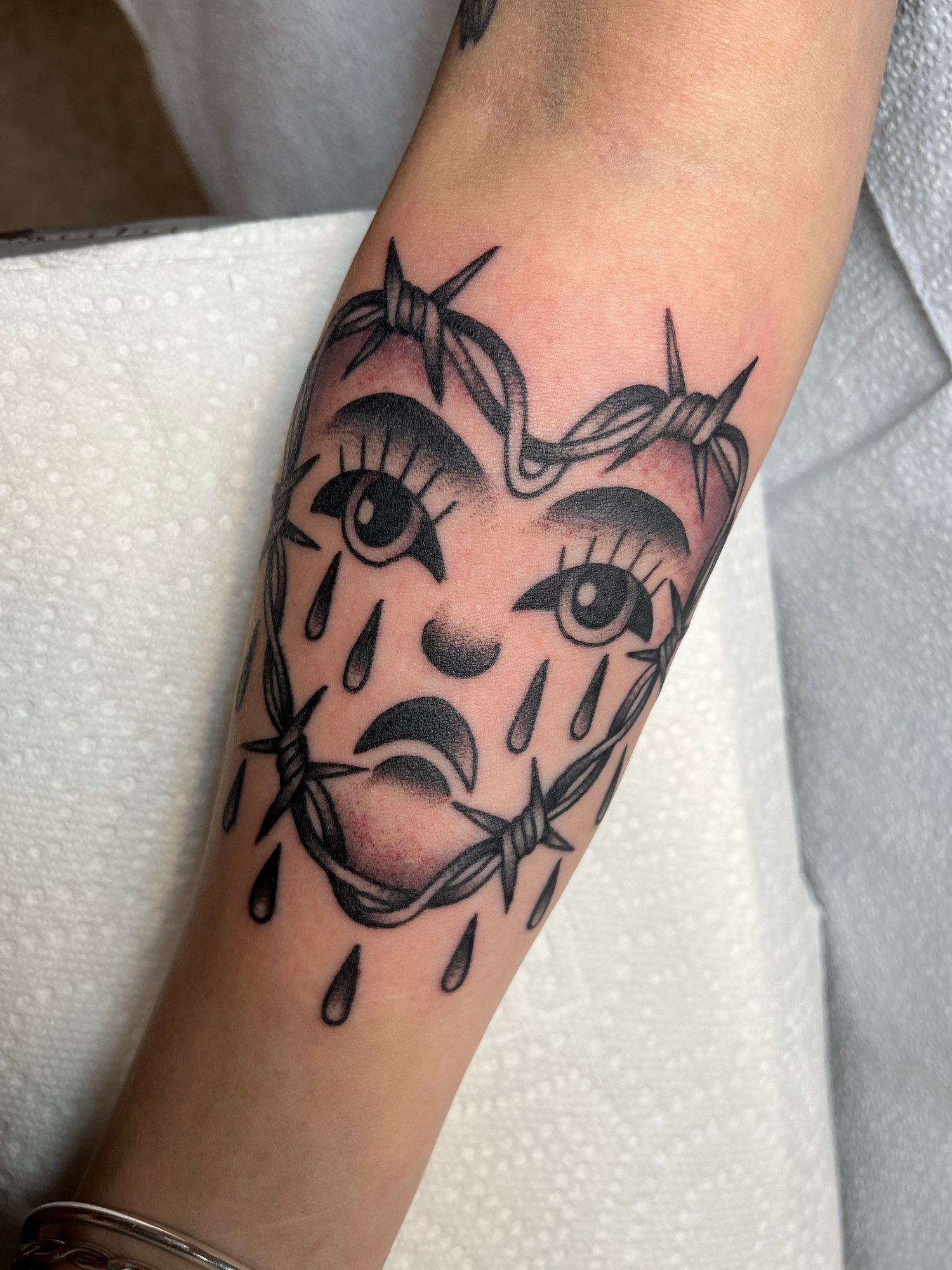A person has a tattoo of a crying heart with barbed wire around it.