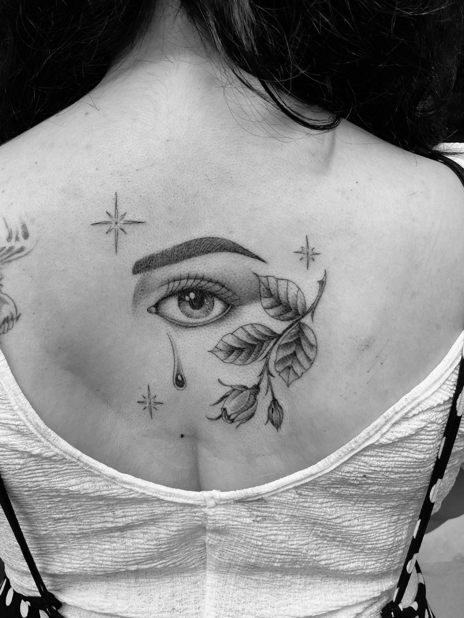 A black and white photo of a woman 's back with a tattoo of an eye and leaves.